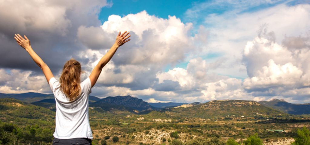 Mujer con los brazos en alto, disfrutando del paisaje panorámico de montaña en la Ardèche.
